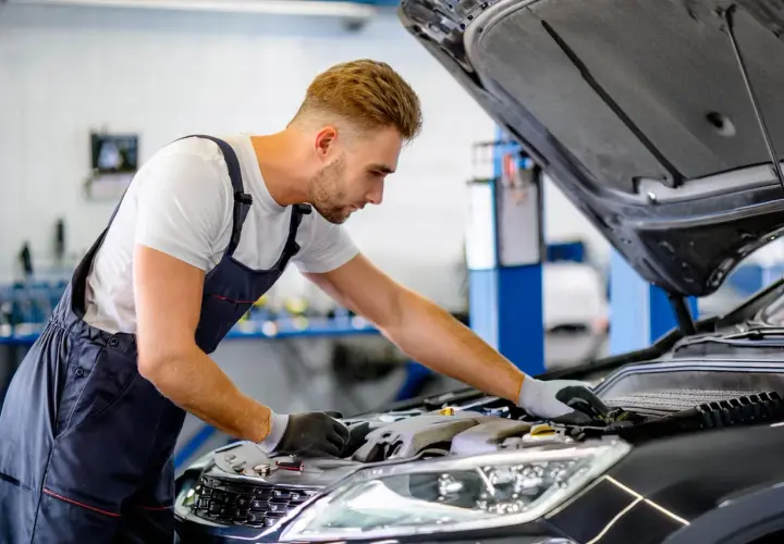 Mécanicien concentré sur le moteur d'une voiture, cherchant une astuce pour essuie glace en panne.