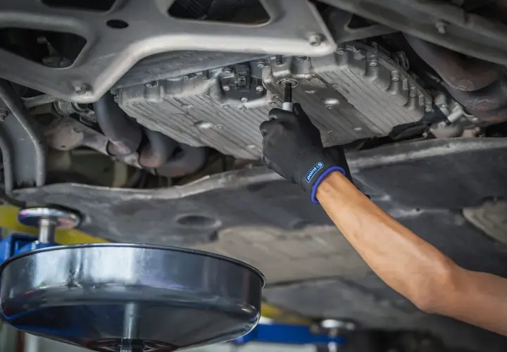 Main d'un mécanicien en gant noir dévissant le bouchon de vidange d'une voiture diesel. Le prix de la vidange voiture diesel est une préoccupation pour de nombreux propriétaires.
