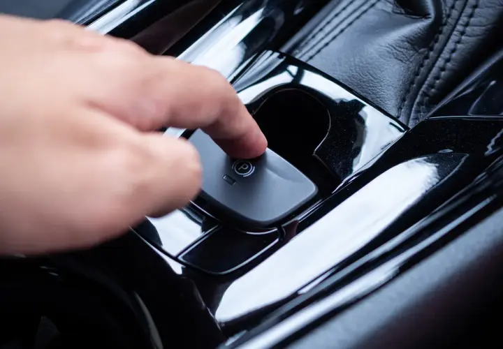 Main d'une personne appuyant sur le bouton du frein à main automatique. Voici comment débloquer un frein à main automatique.