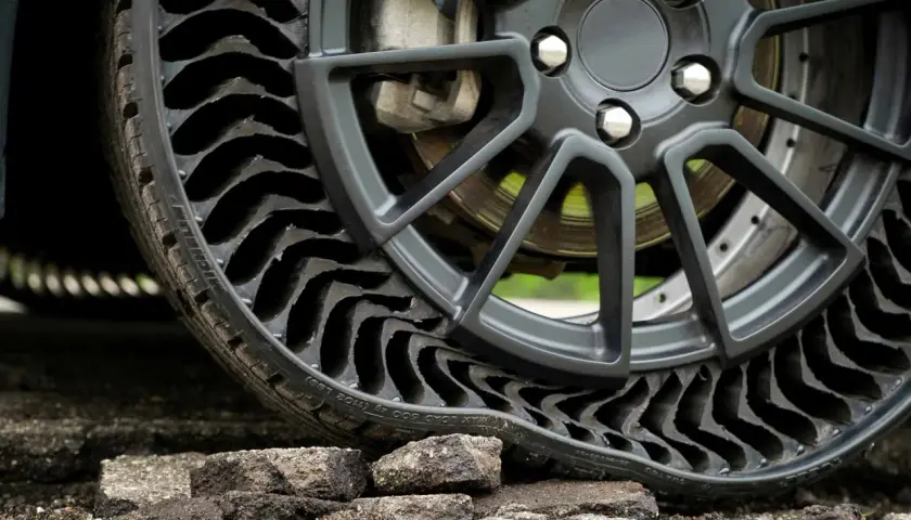 Gros plan sur une roue de voiture avec un pneu increvable, composé de multiples alvéoles noires, posé sur un sol dégradé.