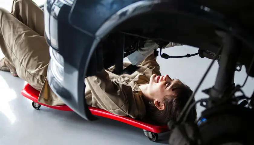 Mécanicienne travaillant sous une voiture, utilisant un chariot pour accéder à une pièce de réemploi.