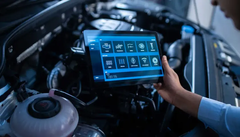 Un technicien utilise une tablette pour un suivi entretien voiture gratuit, diagnostiquant le moteur et les systèmes.