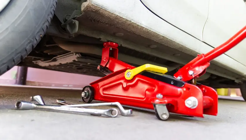 Un cric rouge est utilisé pour soulever une voiture. Des clés sont posées au sol, prêtes à être utilisées pour changer une roue.