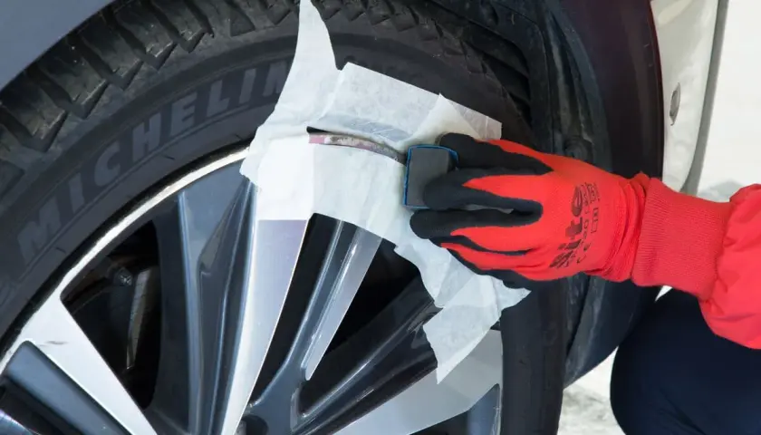 Main d'une personne portant un gant rouge et noir, utilisant un produit pour réparer jante alu.