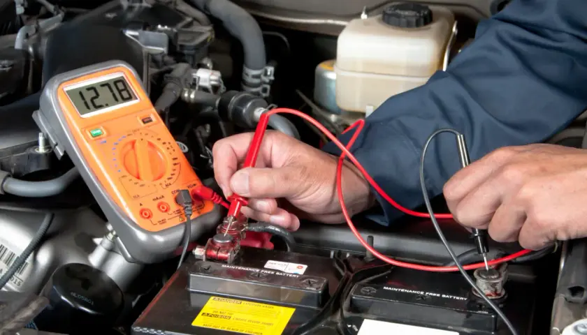 Un mécanicien vérifie la tension de la batterie d'une Mini Cooper. L'emplacement de la batterie est sous le capot, accessible pour le diagnostic.