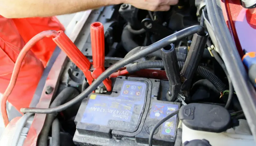 Comment brancher un booster de batterie : les pinces rouges et noires sont connectées à la batterie d'une voiture.