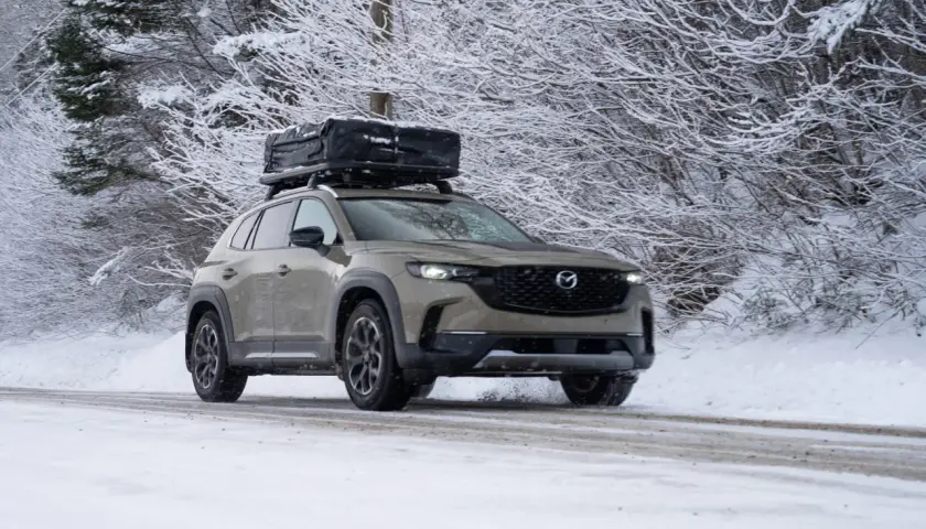 Un SUV gris roule sur une route enneigée, prêt à affronter l'hiver avec un coffre de toit chargé.