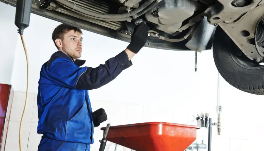 Mécanicien en bleu effectuant la vidange d'une voiture, prêt à changer l'huile. Savoir quand faire vidange voiture est essentiel.