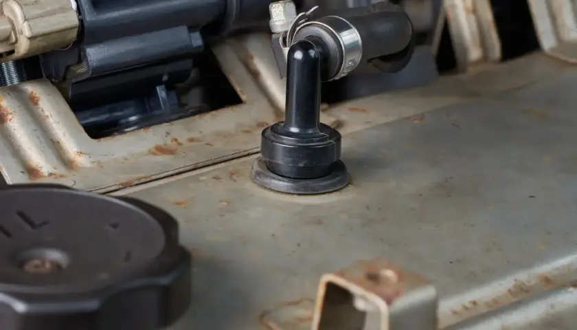 Détail d'un moteur de voiture, avec un tuyau noir fixé par un collier métallique. On aperçoit une pièce en caoutchouc noir, peut-être pour supprimer le reniflard d'huile.