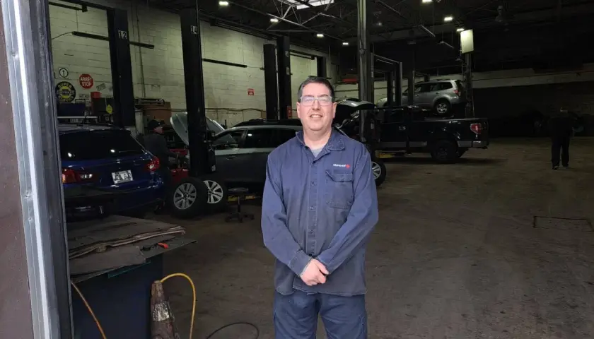 Homme souriant dans un garage libre service pour réparer soi-même. Plusieurs voitures sur des ponts élévateurs.