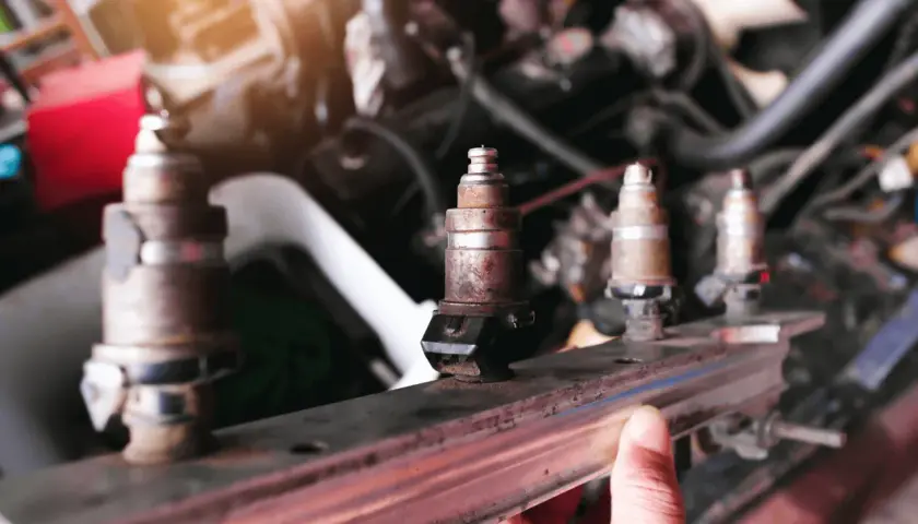 Un mécanicien examine un injecteur qui claque, rouillé et usé, prêt à être remplacé dans le moteur d'une voiture.