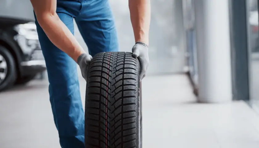 Un mécanicien en bleu tient un pneu d'hiver, une sous-marque Michelin, prêt pour le montage.