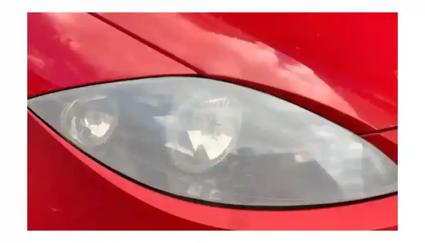 Phare de voiture rouge terni, prêt pour un nettoyage efficace avec du vinaigre blanc.