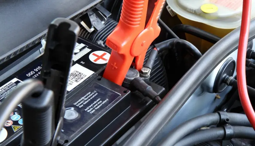 Pinces rouges connectées à la batterie pour recharger batterie voiture. Le niveau d'acide est indiqué.