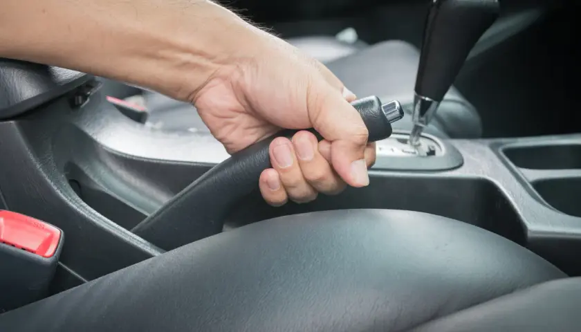 Main d'un conducteur actionnant le frein à main bloqué dans une voiture.