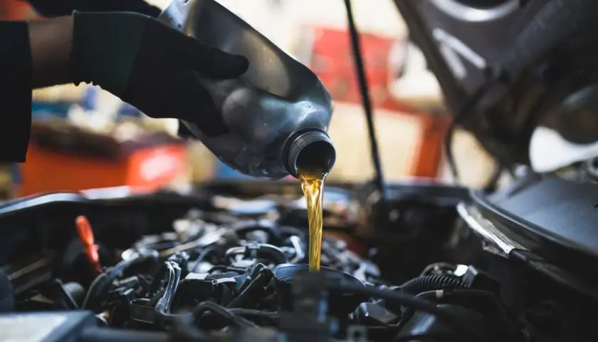 Main d'un mécanicien versant de l'huile neuve dans le moteur d'une Dacia Sandero lors d'une vidange.