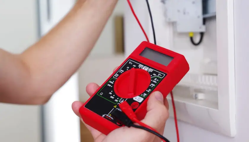 Main rouge pour tester un fusible voiture avec un multimètre.