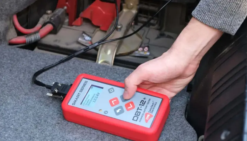 Utilisation d'un testeur de batterie avancé pour savoir comment tester une batterie sans multimètre. L'appareil affiche 12.14V.