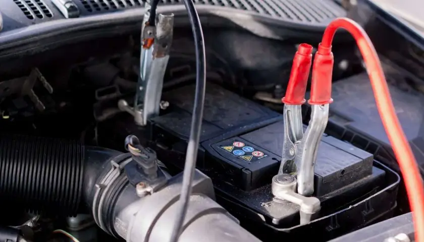 Pinces de démarrage connectées à une batterie de voiture, signe d'une conséquence batterie faible voiture.
