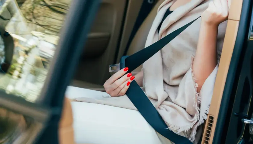 Main tenant, une femme aux ongles rouges s'apprête à changer ceinture de sécurité dans une voiture de luxe.