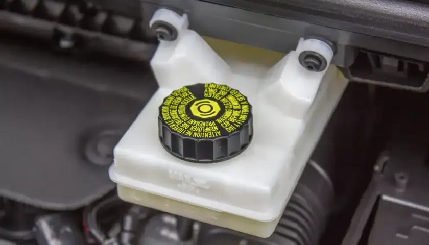 Réservoir de liquide de frein avec bouchon noir et jaune. Le niveau du liquide est visible, indiquant la nécessité d'un contrôle du liquide de frein.