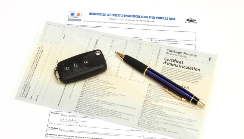 Carte grise, clé de voiture et stylo sur un document officiel.