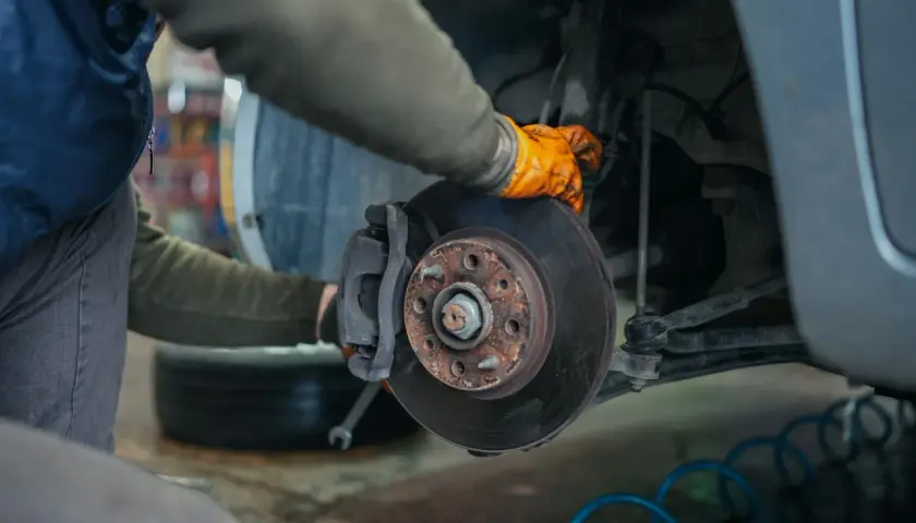 Mécanicien inspectant un disque de frein rouillé, peut-être une plaquette de frein glacée à remplacer.