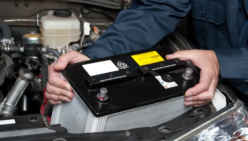 Un mécanicien installe une nouvelle batterie de voiture. Le poids de la batterie est géré avec soin.