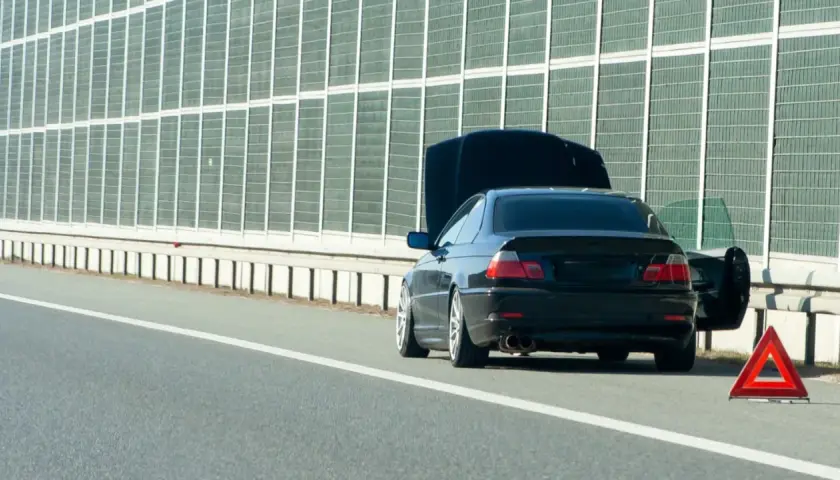 Panne sur l'autoroute. Capot ouvert, portière conducteur ouverte, triangle de signalisation rouge. Un entretien véhicule s'impose.