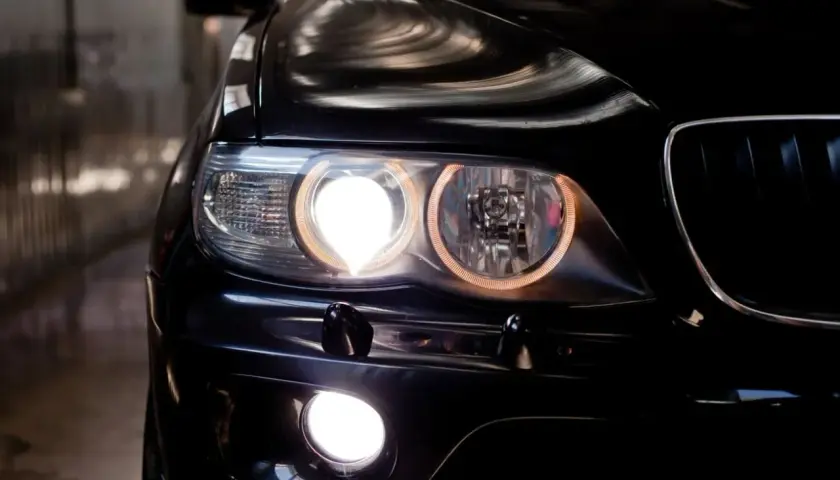Gros plan sur l'avant d'une voiture noire, les feux de position allumés, créant une lumière intense et des reflets sur la carrosserie.