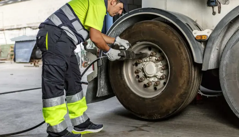 Un mécanicien en tenue de travail effectue le couple serrage roue voiture d'un camion avec une clé à chocs.