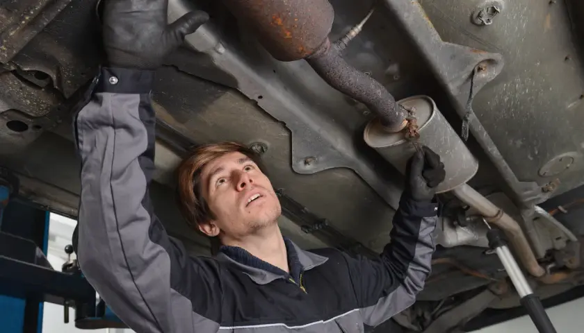 Mécanicien inspectant le pot catalytique d'une voiture, sous le véhicule.