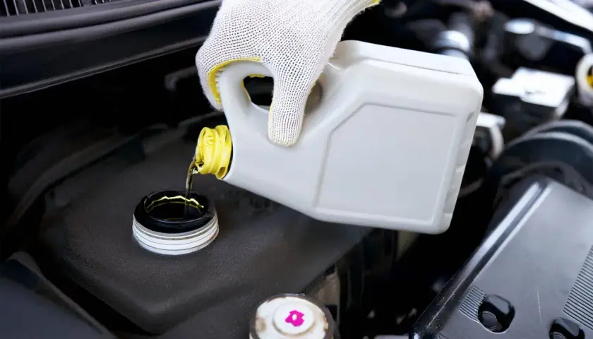 Main d'un mécanicien en gant blanc versant du liquide de frein neuf dans le réservoir. Le prix du changement de liquide de frein est un entretien essentiel.
