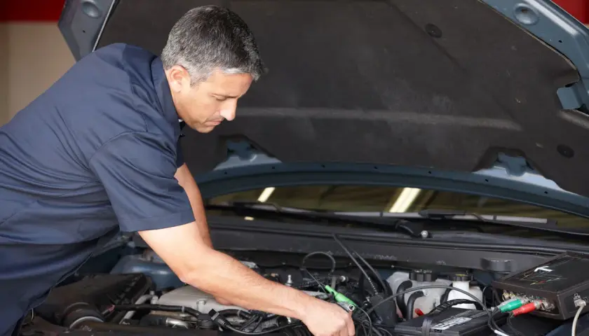Mécanicien diagnostiquant un problème de démarrage à chaud sur un moteur de voiture avec un appareil électronique.