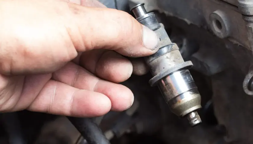 Main d'un mécanicien tenant un injecteur diesel sale, prêt à nettoyer injecteur diesel soi-même.