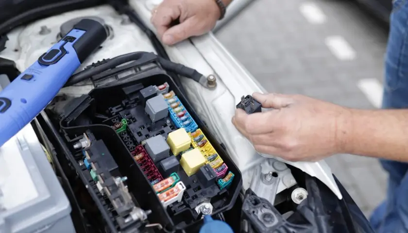 Un mécanicien examine le boîtier de fusibles d'une voiture, cherchant la cause d'un problème électrique. Il tient un relais dans sa main.