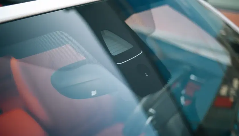 Vue rapprochée du pare-brise d'une voiture, montrant un capteur de luminosité et d'autres éléments électroniques.