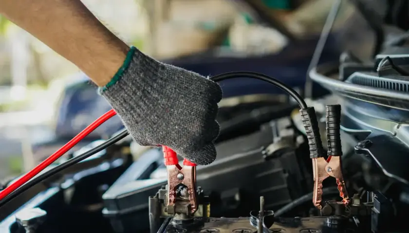 Main tenant un câble pour démarrer une voiture. La pince rouge est connectée à la batterie.