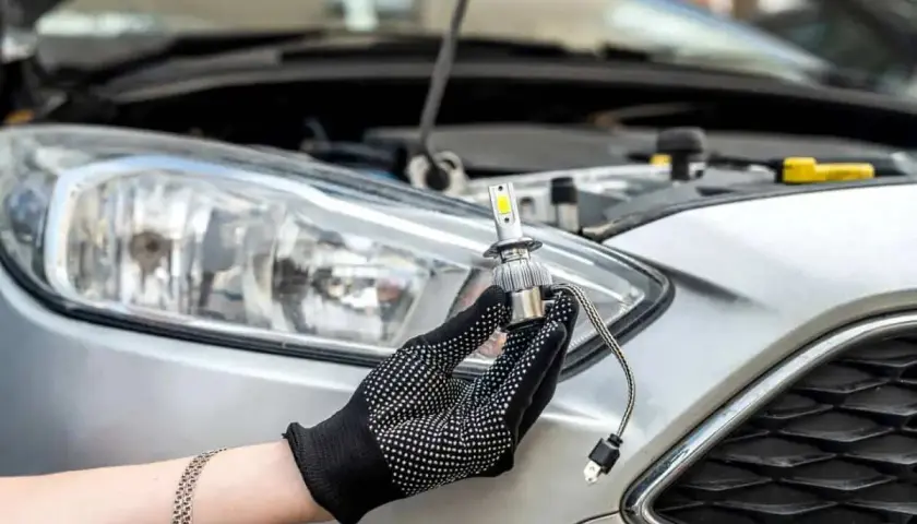 Main tenant une ampoule LED neuve, prêt à changer les ampoules de phare d'une voiture argentée.