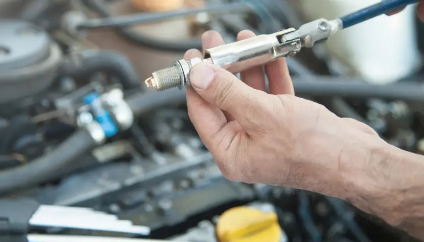 Main d'un mécanicien tenant une bougie d'allumage, prête à être installée dans le moteur d'une voiture.