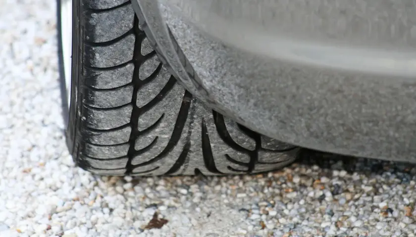 Gros plan sur un pneu de voiture usé, posé sur des graviers. J'espère que mes pneus font du bruit quand je roule, car ils sont en fin de vie !