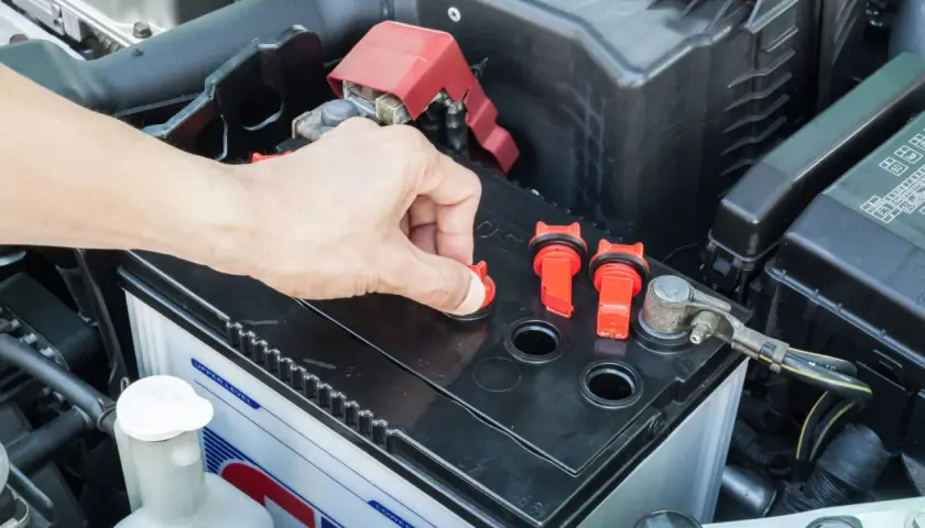 Main d'une personne ouvrant un bouchon sur une batterie de voiture, peut-être pour vérifier le niveau d'eau pour batterie.