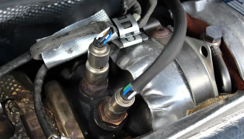 Sonde lambda défectueuse : câblage visible, connecteurs et partie métallique rouillée. Un symptôme de problème moteur.