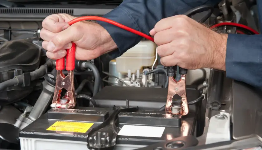 Mains de mécanicien connectant des câbles de démarrage à une batterie de voiture. On peut charger une batterie sans la débrancher.