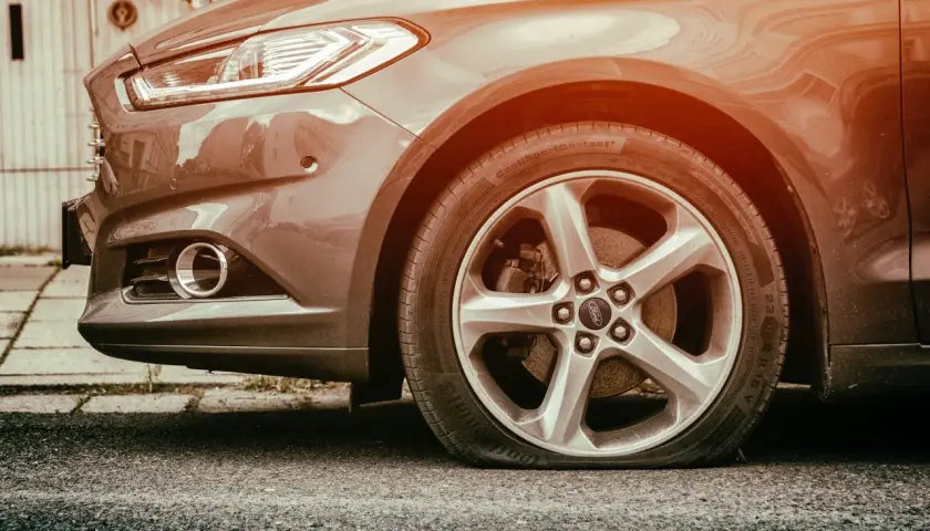 Gros plan sur une roue de voiture Ford avec un pneu crevé, le flanc complètement à plat sur l'asphalte. Une vraie galère !