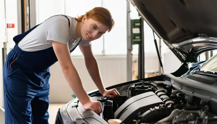 Mécanicien souriant vérifiant le moteur d'une Seat Ibiza ouverte. Il porte une combinaison bleue.