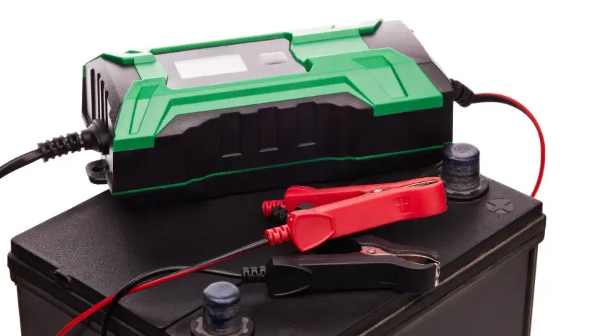 Chargeur de batterie vert et noir connecté à une batterie de voiture. Idéal pour le maintien de charge batterie sans débrancher.