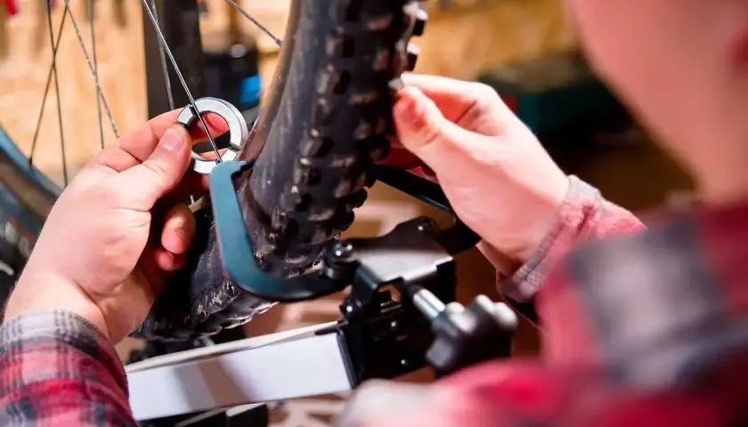Mains ajustant un outil sur la roue voilée d'un vélo, prêt pour la réparation.