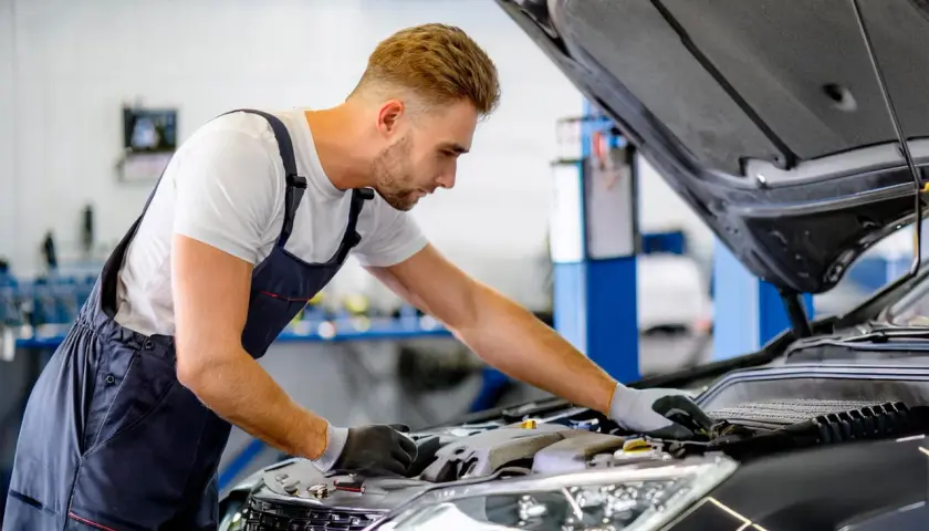 Mécanicien concentré sur le moteur d'une voiture, cherchant une astuce pour essuie glace en panne.