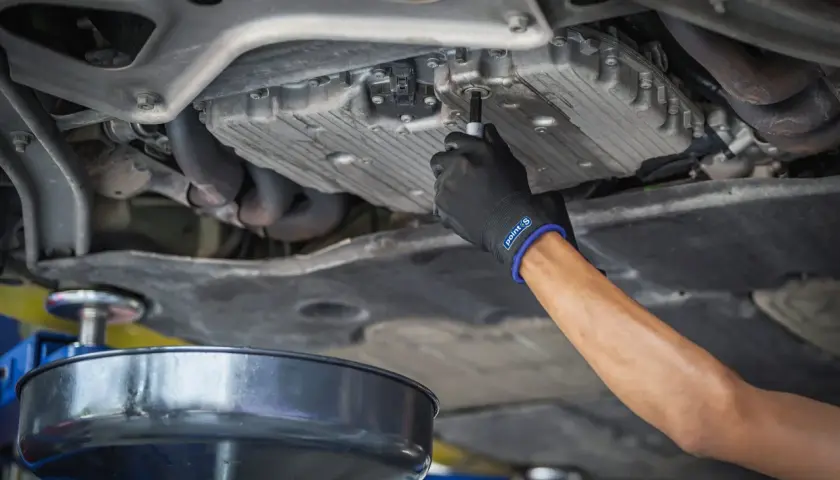 Main d'un mécanicien en gant noir dévissant le bouchon de vidange d'une voiture diesel. Le prix de la vidange voiture diesel est une préoccupation pour de nombreux propriétaires.